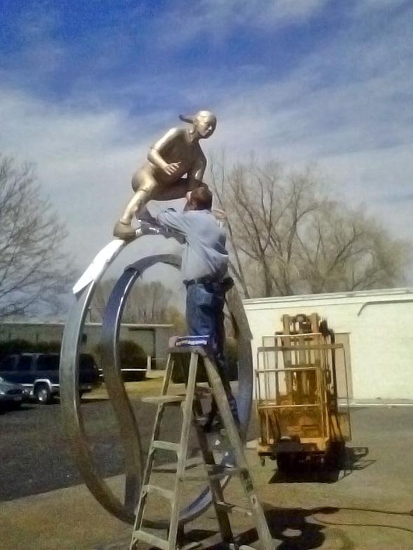 Man on a ladder working on the base of the sculpture