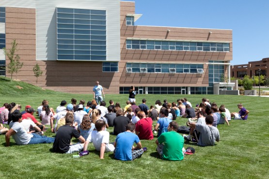 Freshmen Seminar students sit on the West Lawn grass with The Osborne Center behind them