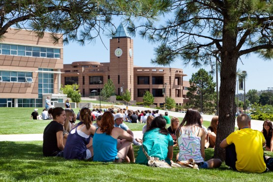 Students sit on the grass with El Pomar Center bell tower behind them
