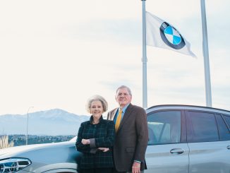 Phil and Ann Winslow standing in front of a car with a BMW flag and Pikes Peak in the background
