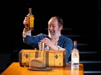 An actor holds a bottle on a stage set