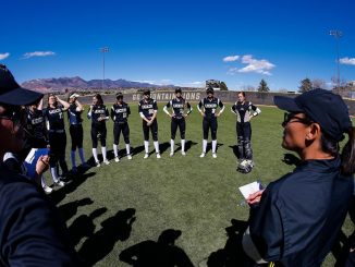 The softball team gathers in a circle for instructions from the coach at Mountain Lion Field