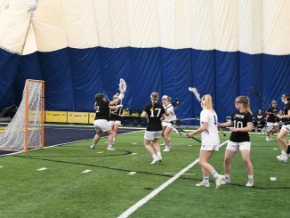 Lacrosse players in front of a goal in an inflatable building.