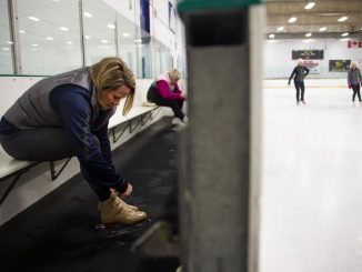 A skater ties her skates at the end of an ice rink