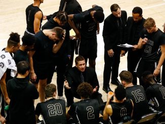 Head Coach Jeff Culver surrounded by the men's basketball team on the team bench during a timeout.