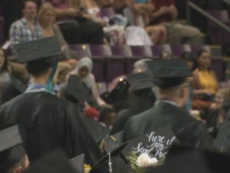 Students stand during the 2019 spring commencement ceremony