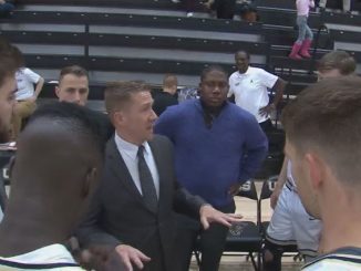 A screenshot of head coach Jeff Culver in a men's basketball team huddle on the court