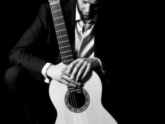 A black and white photo of Colin McAlister holding a guitar