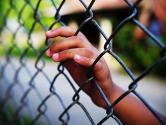 A hand rests on a chain link fence