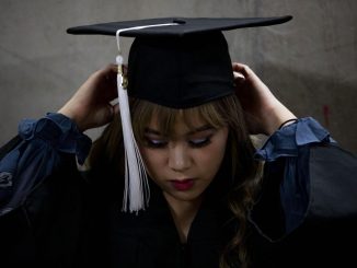 A graduate fits her mortar board in a hallway