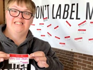 Nick Harmon holds a sticker in front of a "Don't Label Me" banner
