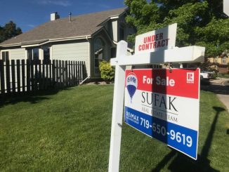 A realtor's sign in a yard in front of a house