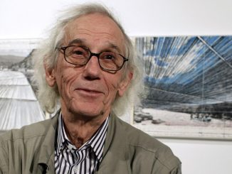 Christo stands in front of a piece of art in a Denver gallery