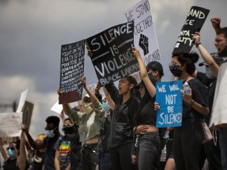 Students protesting and holding signs by a campus sign