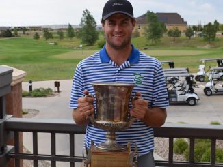 Colin Prater holds a trophy on a golf course