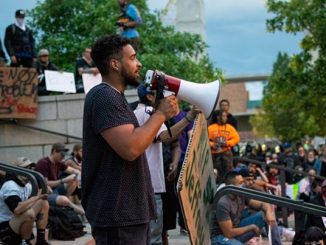 A person with a bullhorn stands on the steps in a crowd in front of Colorado Springs City Hall