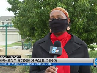 Stephany Rose Spauling holds a microphone while being interviewed with a face covering