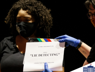 A person holds a clapboard while an actor waits to begin