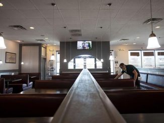 A person wipes down a table in an empty restaurant