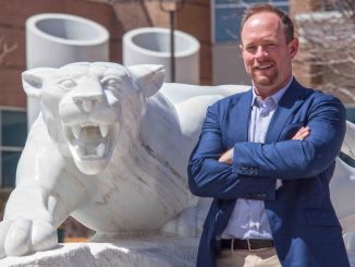 Craig Smith with his arms folder in front of the mountain lion statue