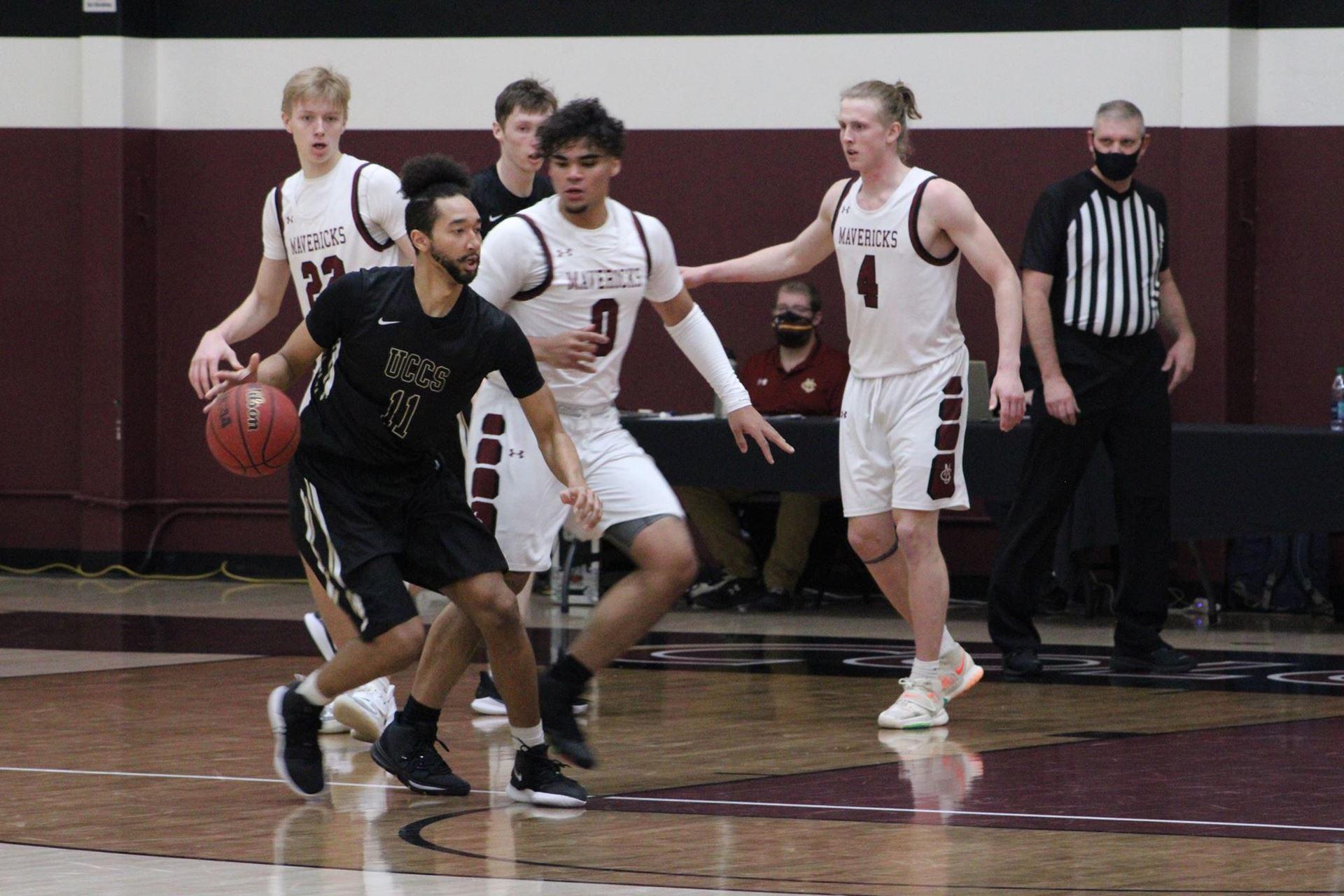 Geoff Kelly dribbling the basketball against Colorado Mesa defenders