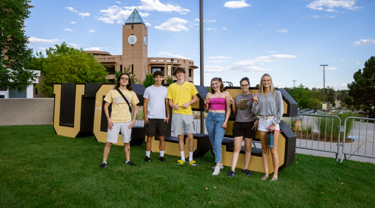 A group of students stand in front of the giant UCCS letters on the West Lawn.