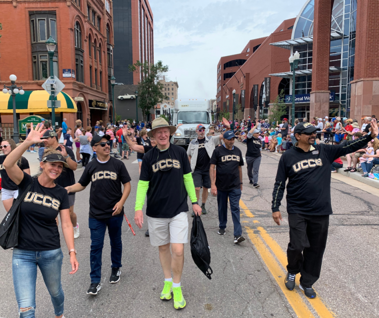 People wearing UCCS shirts walk down the middle of the road during a parade.