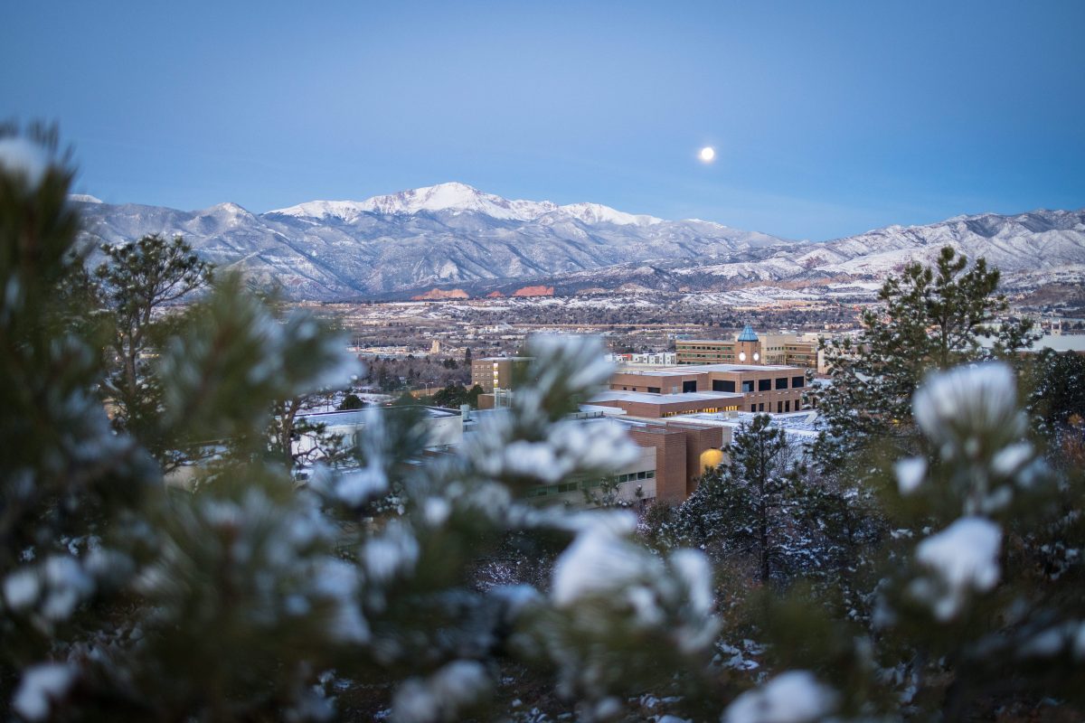 Panoramic view of a snow-covered UCCS campus, with a full moon setting over Pikes Peak. Photo by Jeffrey M Foster